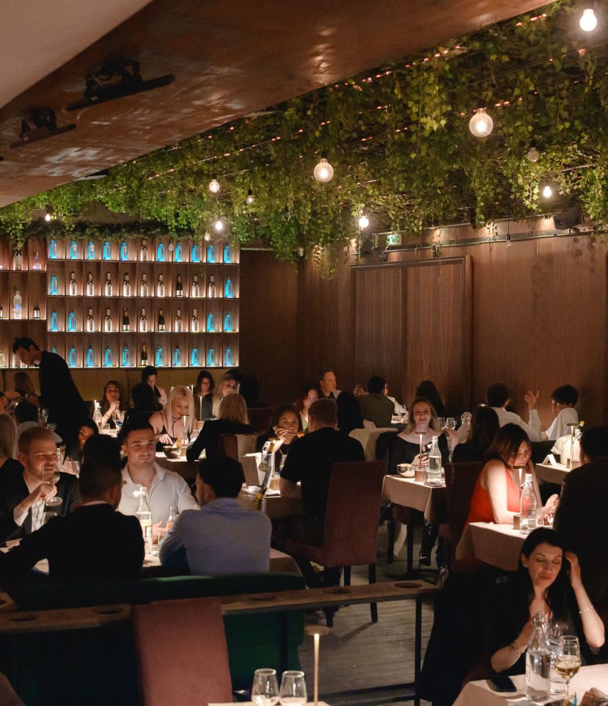 La sala del ristorante piena, i tavoli apparecchiati sotto il verde appeso